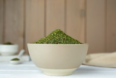 Photo of Dried dill in bowl on white wooden table