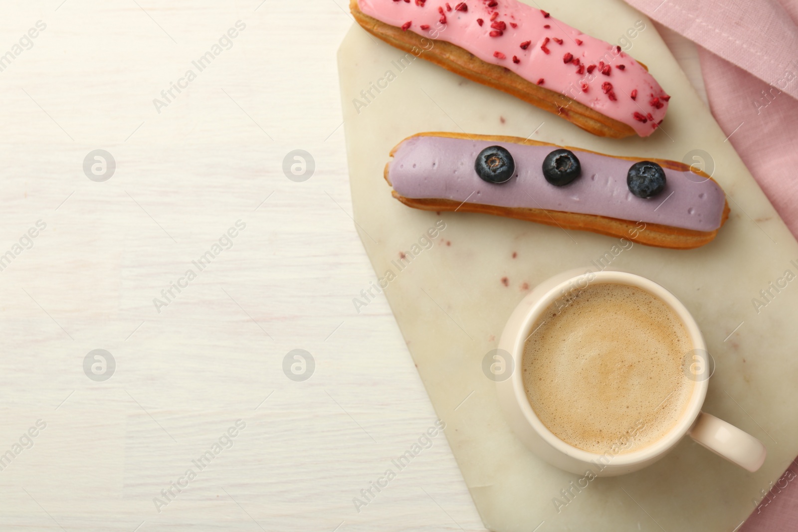 Photo of Cup of coffee and delicious eclairs covered with glaze on white wooden table, top view. Space for text