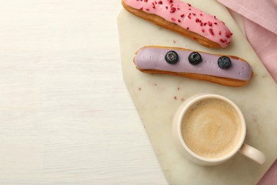 Photo of Cup of coffee and delicious eclairs covered with glaze on white wooden table, top view. Space for text