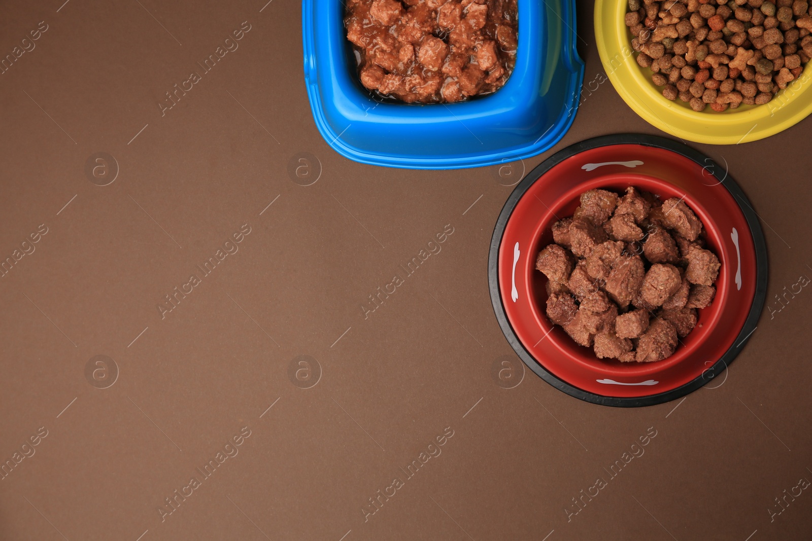 Photo of Dry and wet pet food in feeding bowls on brown background, flat lay. Space for text