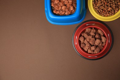 Photo of Dry and wet pet food in feeding bowls on brown background, flat lay. Space for text