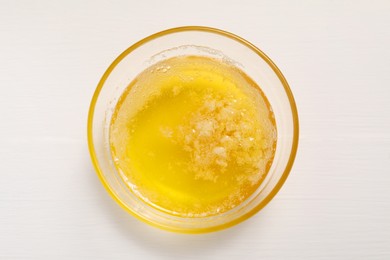 Photo of Melted butter in glass bowl on white wooden table, top view