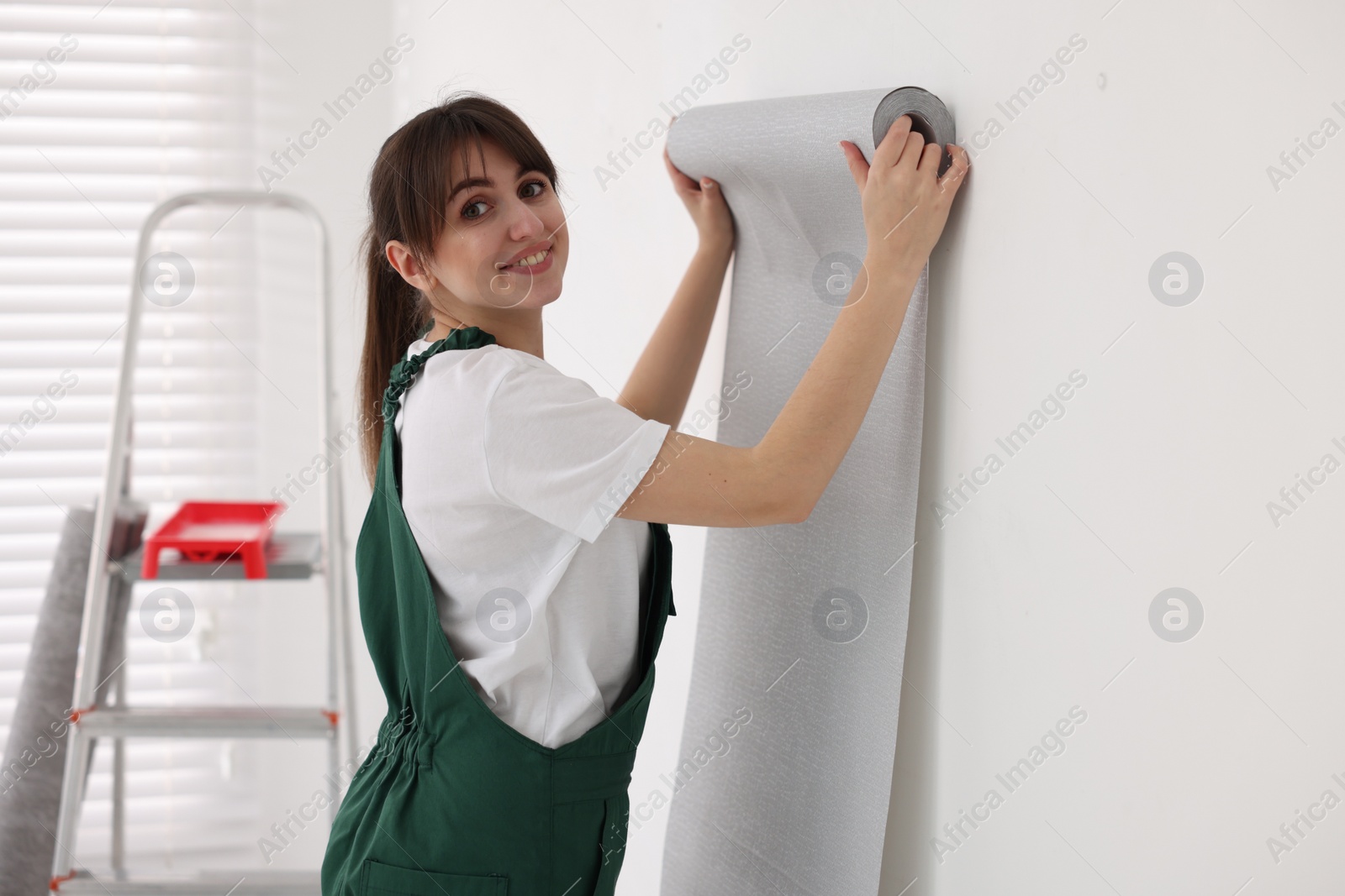 Photo of Woman hanging stylish gray wallpaper in room