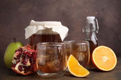 Photo of Tasty kombucha with ice cubes and fruits on wooden table