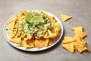 Plate of delicious mexican nachos chips with guacamole sauce and lime on grey table