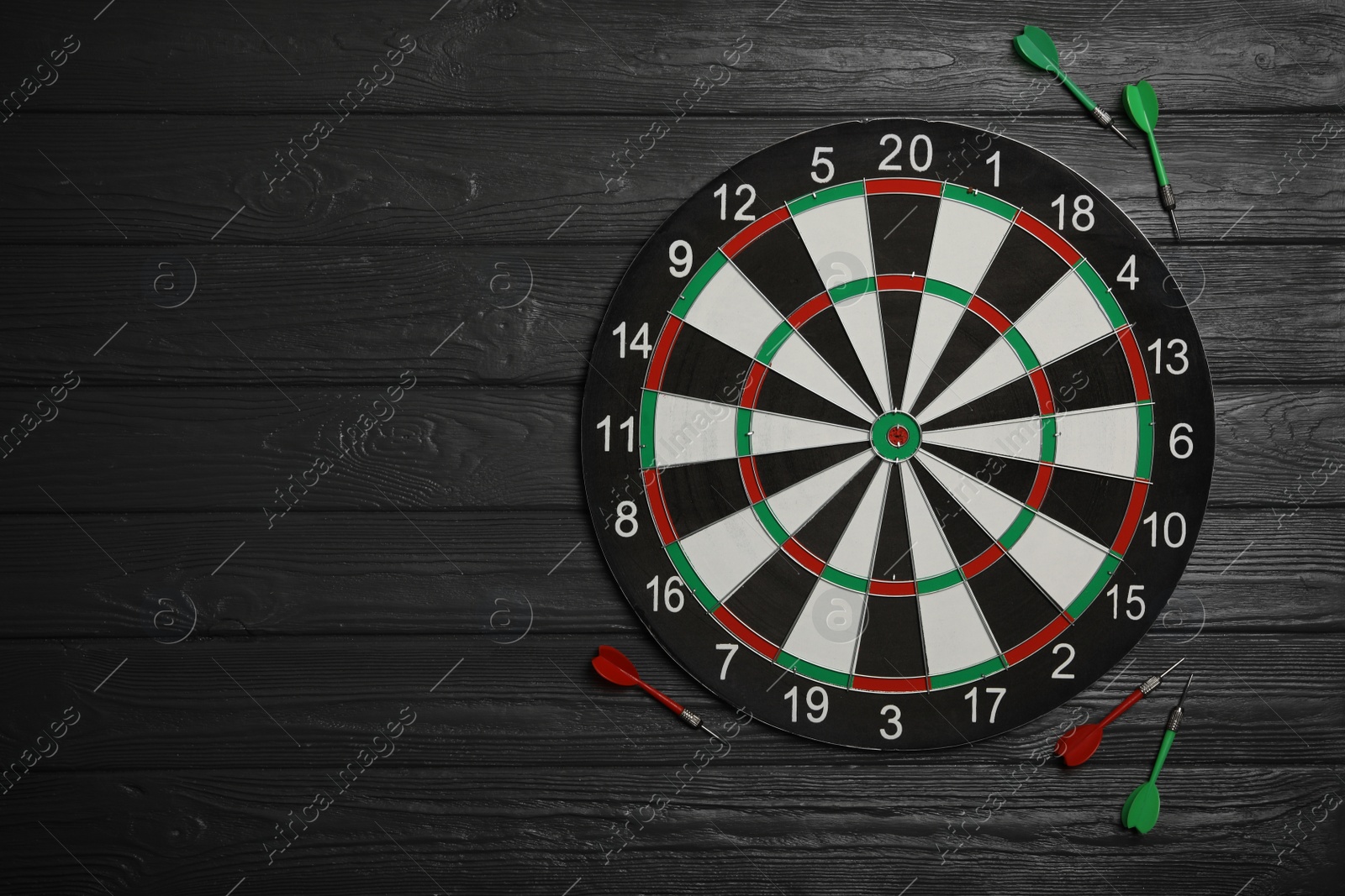 Photo of Dart board with color arrows on black wooden background, top view. Space for text