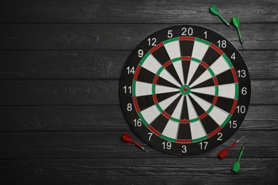 Dart board with color arrows on black wooden background, top view. Space for text