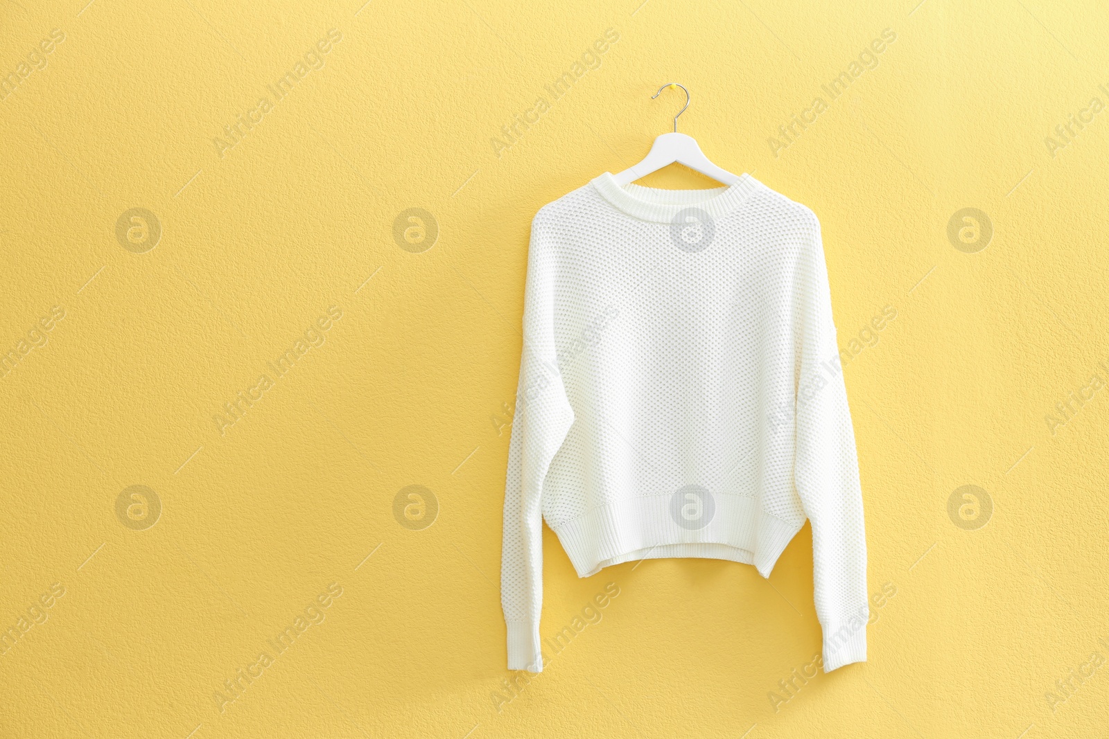 Photo of Hanger with stylish sweater on yellow wall. Space for text