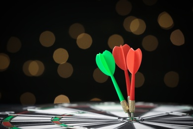 Photo of Arrows hitting target on dart board against blurred lights. Space for text