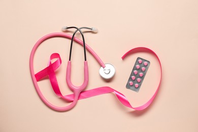 Pink ribbon, stethoscope and pills on beige background, flat lay. Breast cancer awareness