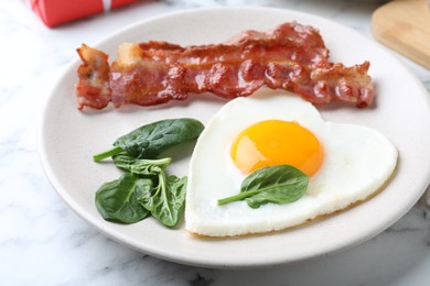 Photo of Romantic breakfast with fried bacon and heart shaped egg on white marble table, closeup. Valentine's day celebration