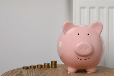 Piggy bank and stacked coins on wooden table near heating radiator, space for text