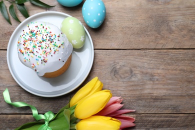 Photo of Flat lay composition with Easter cake and painted eggs on wooden table. Space for text