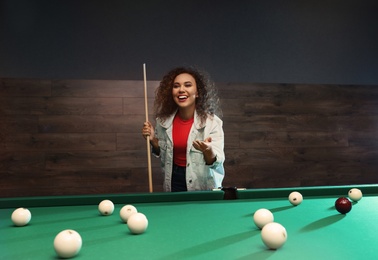 Photo of Young African-American woman with cue near billiard table indoors