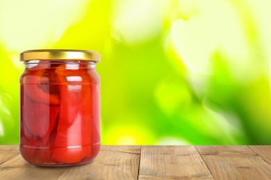 Image of Jar of pickled bell peppers on wooden table against blurred background, space for text