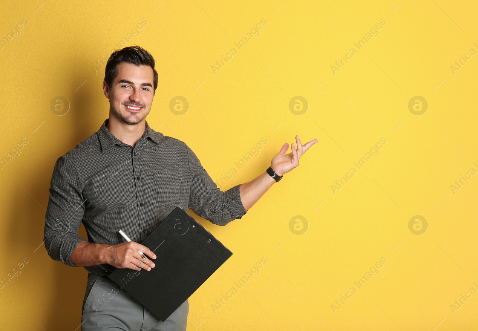 Photo of Young male teacher with clipboard on yellow background. Space for text