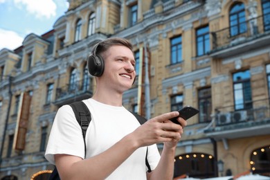 Photo of Smiling man in headphones using smartphone outdoors. Space for text