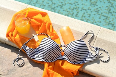 Photo of Glass of refreshing drink and different beach accessories near outdoor swimming pool on sunny day