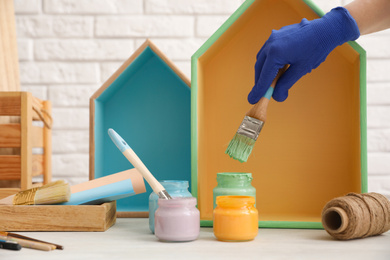 Photo of Decorator dipping brush into jar of green paint at white table, closeup