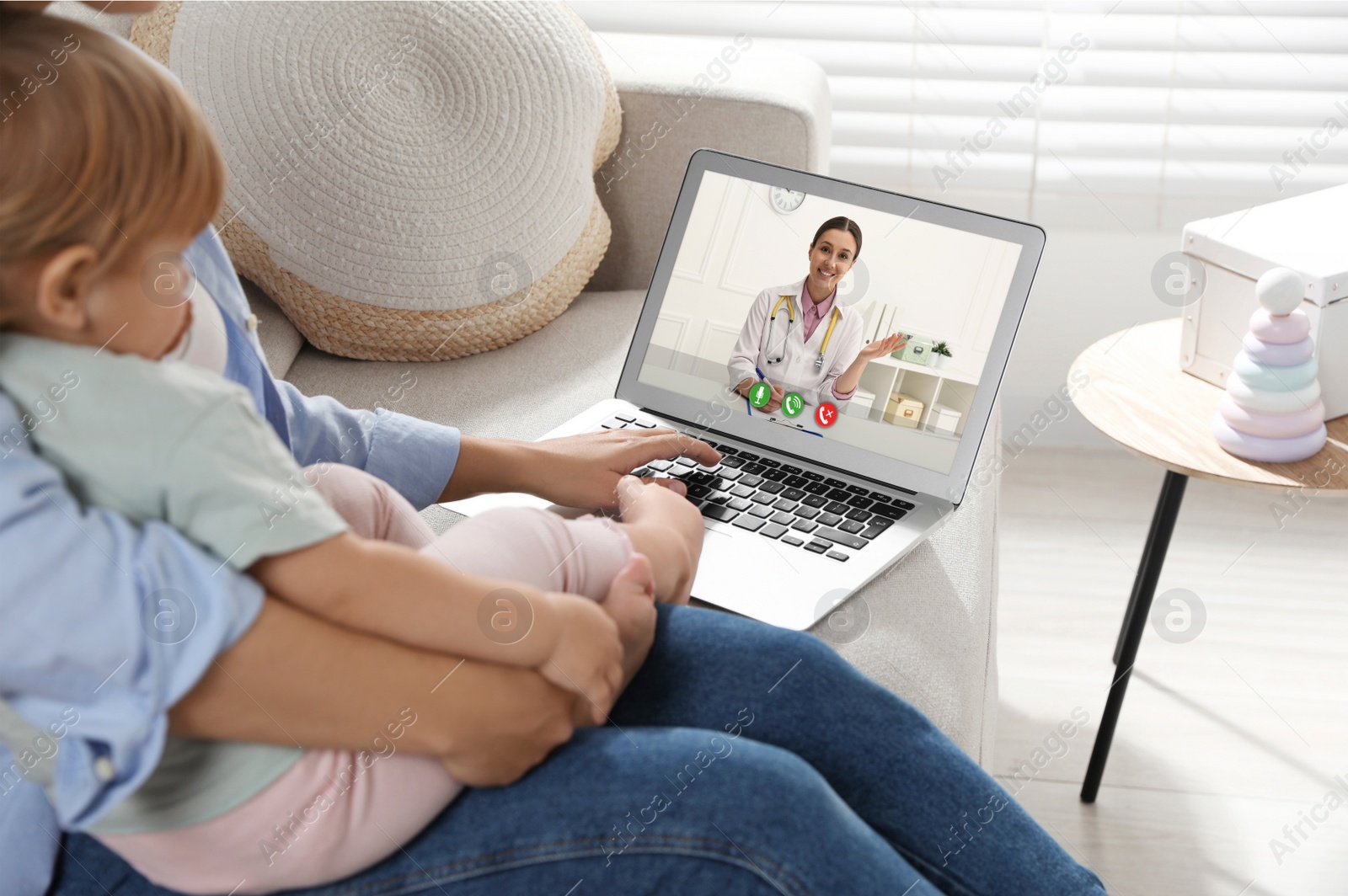 Image of Mother and daughter having online consultation with pediatrician via laptop on sofa at home