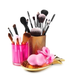 Photo of Holders with makeup brushes and sponge of professional artist on white background