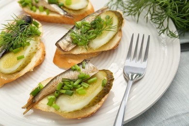 Photo of Delicious sandwiches with sprats, pickled cucumber, green onion and dill on plate, closeup
