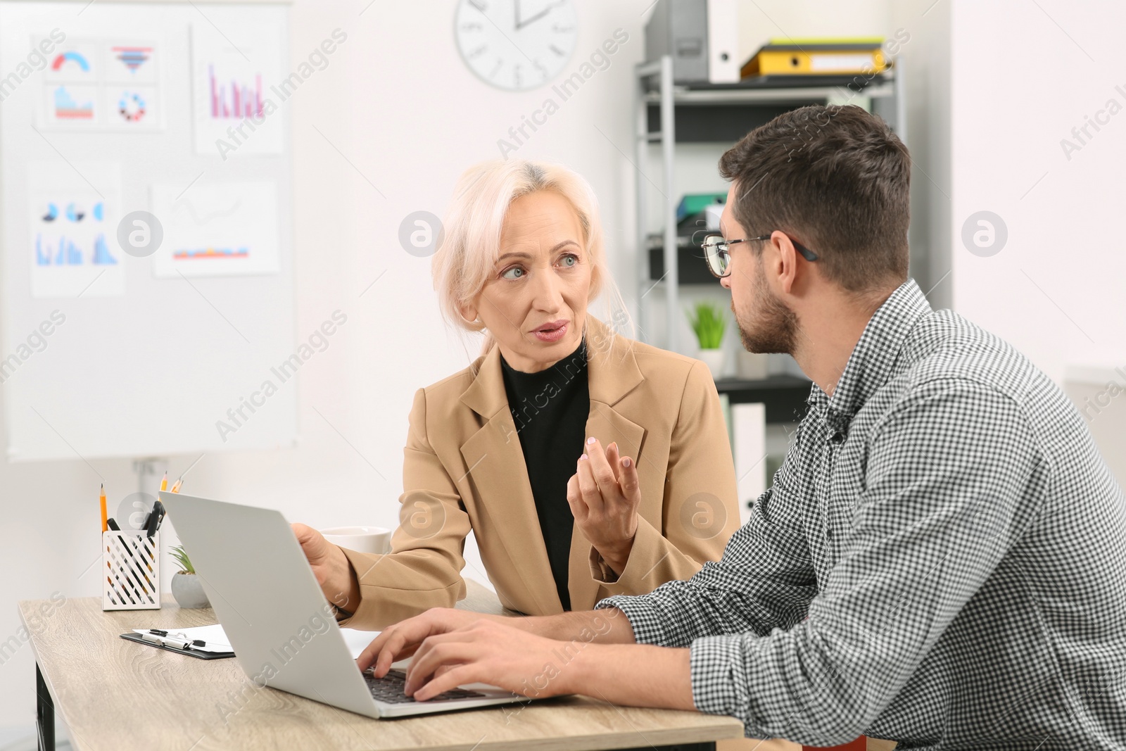 Photo of Boss and employee with laptop discussing work issues at wooden table in office