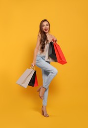 Photo of Stylish young woman with shopping bags on orange background