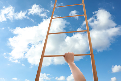 Image of Woman climbing up wooden ladder against blue sky with clouds, closeup