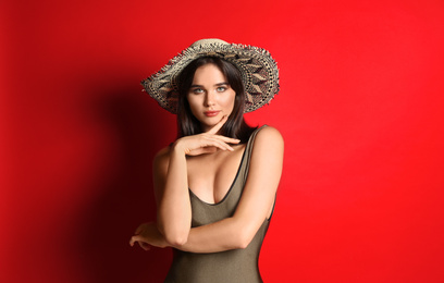 Photo of Beautiful woman in stylish swimsuit and hat on red background