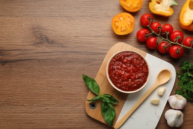 Delicious adjika sauce in bowl and ingredients on wooden table, flat lay. Space for text