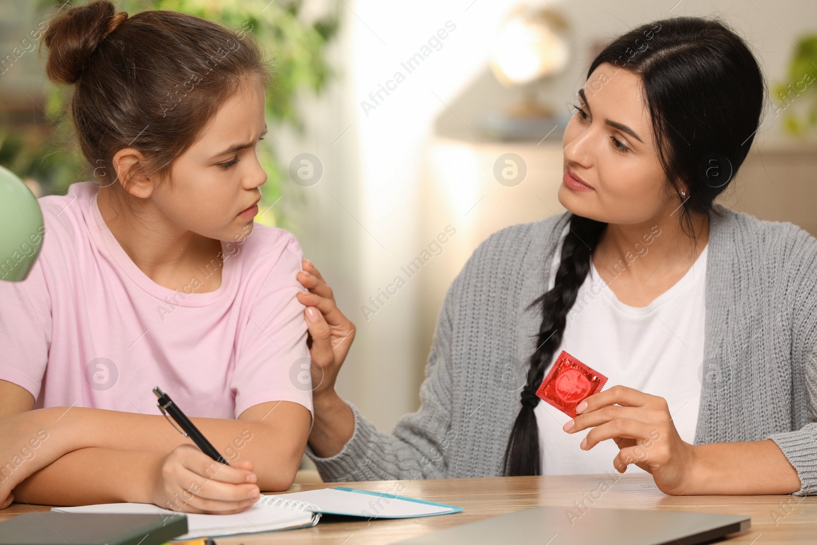 Photo of Mother talking with her teenage daughter about contraception while she doing homework at home. Sex education concept