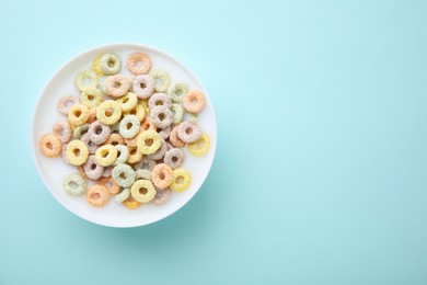 Photo of Tasty colorful cereal rings and milk in bowl on turquoise background, top view. Space for text