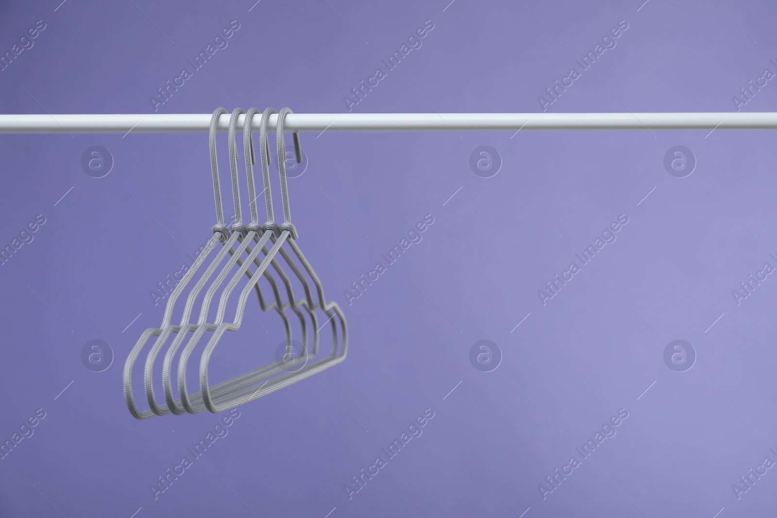 Photo of Empty clothes hangers on rack against purple background. Space for text