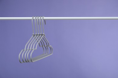 Photo of Empty clothes hangers on rack against purple background. Space for text