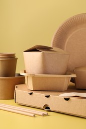 Photo of Eco friendly food packaging. Paper containers and tableware on pale yellow background