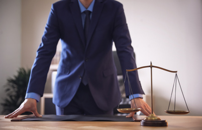 Photo of Male lawyer at table in office, focus on scales of justice