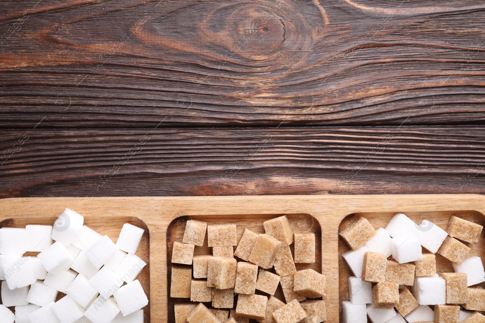 Photo of Tray with brown and white sugar cubes on wooden table, top view. Space for text