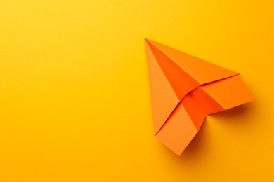 Photo of Handmade orange paper plane on yellow background, top view. Space for text