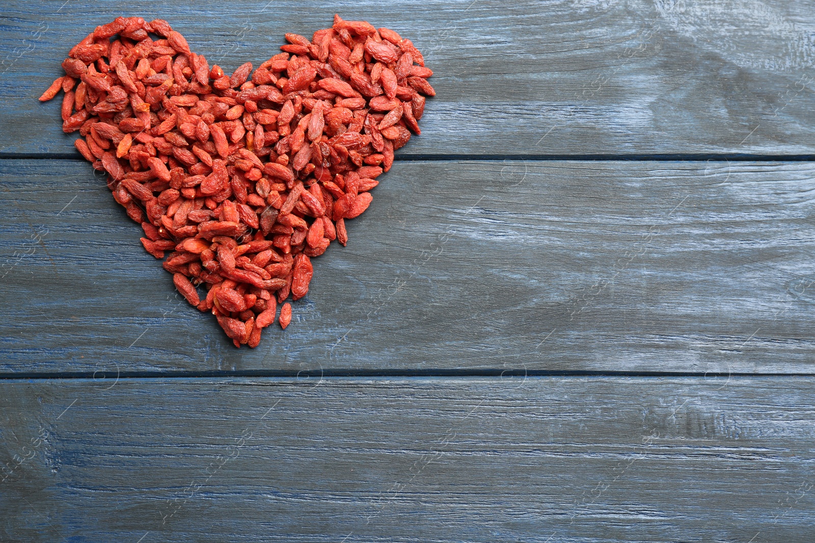 Photo of Heart made of dried goji berries on blue wooden table, top view with space for text. Healthy superfood