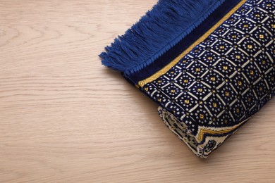 Photo of Muslim prayer rug on wooden table, top view. Space for text