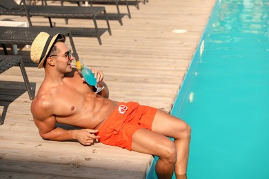 Young man with cocktail near pool on sunny day