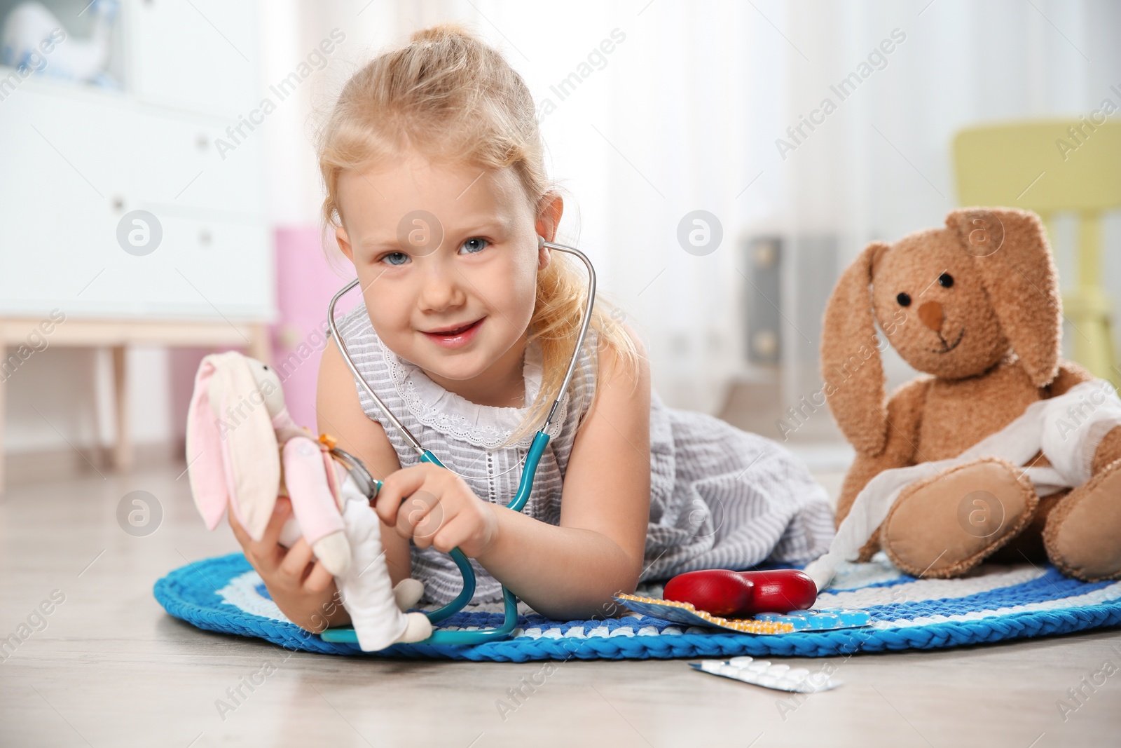 Photo of Cute child imagining herself as doctor while playing with stethoscope and toy bunny at home