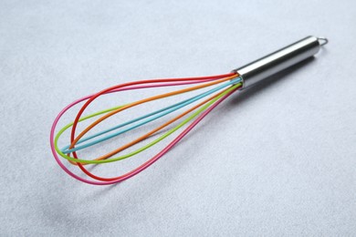 Photo of Bright whisk on gray table, closeup. Kitchen tool