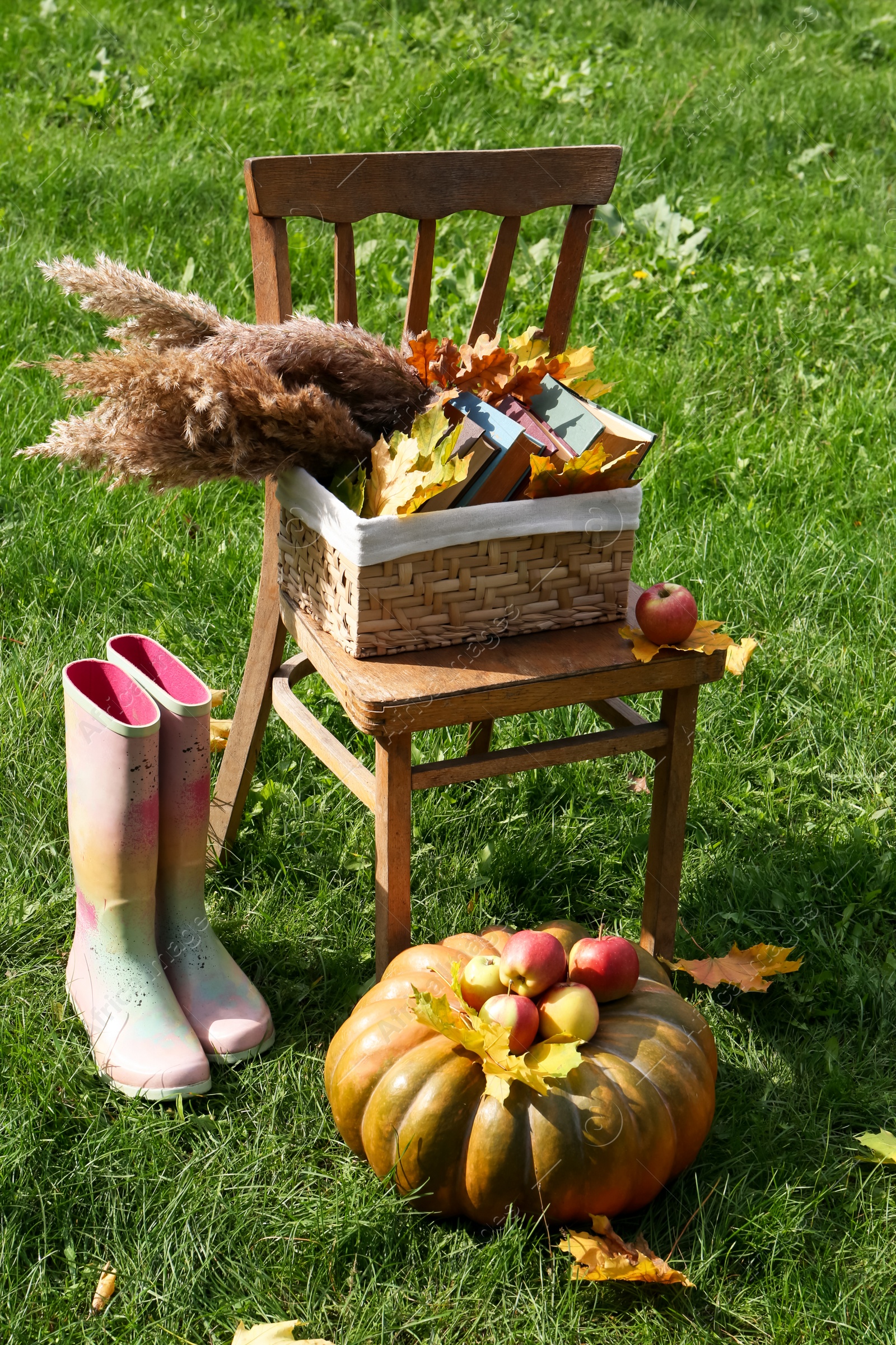 Photo of Rubber boots, chair, pumpkin and apples on green grass outdoors. Autumn atmosphere