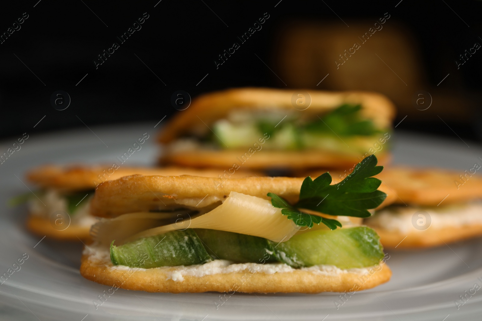 Photo of Delicious crackers with cream cheese, cucumber and parsley on plate, closeup