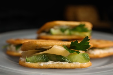 Delicious crackers with cream cheese, cucumber and parsley on plate, closeup