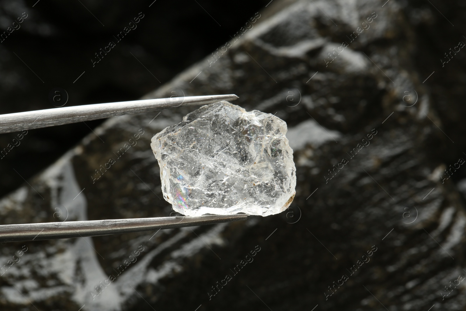 Photo of Tweezers with beautiful shiny diamond over stones, closeup