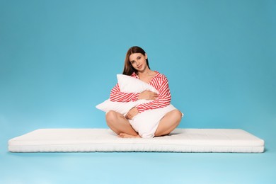 Photo of Young woman on soft mattress holding pillow against light blue background
