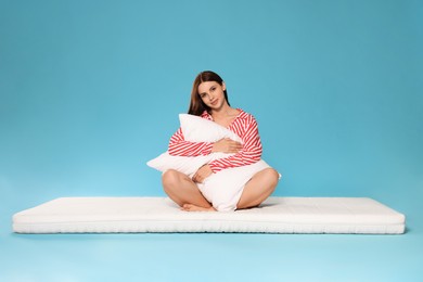 Young woman on soft mattress holding pillow against light blue background